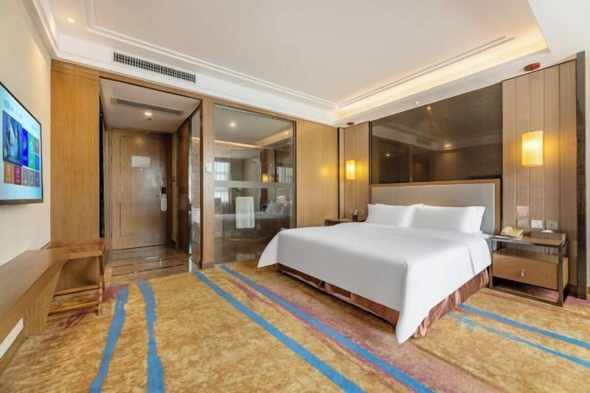 Ein Hotelzimmer mit einem großen Bett, einem Schreibtisch, einem Stuhl, einem Kleiderschrank und einem Badezimmer mit Glastür.