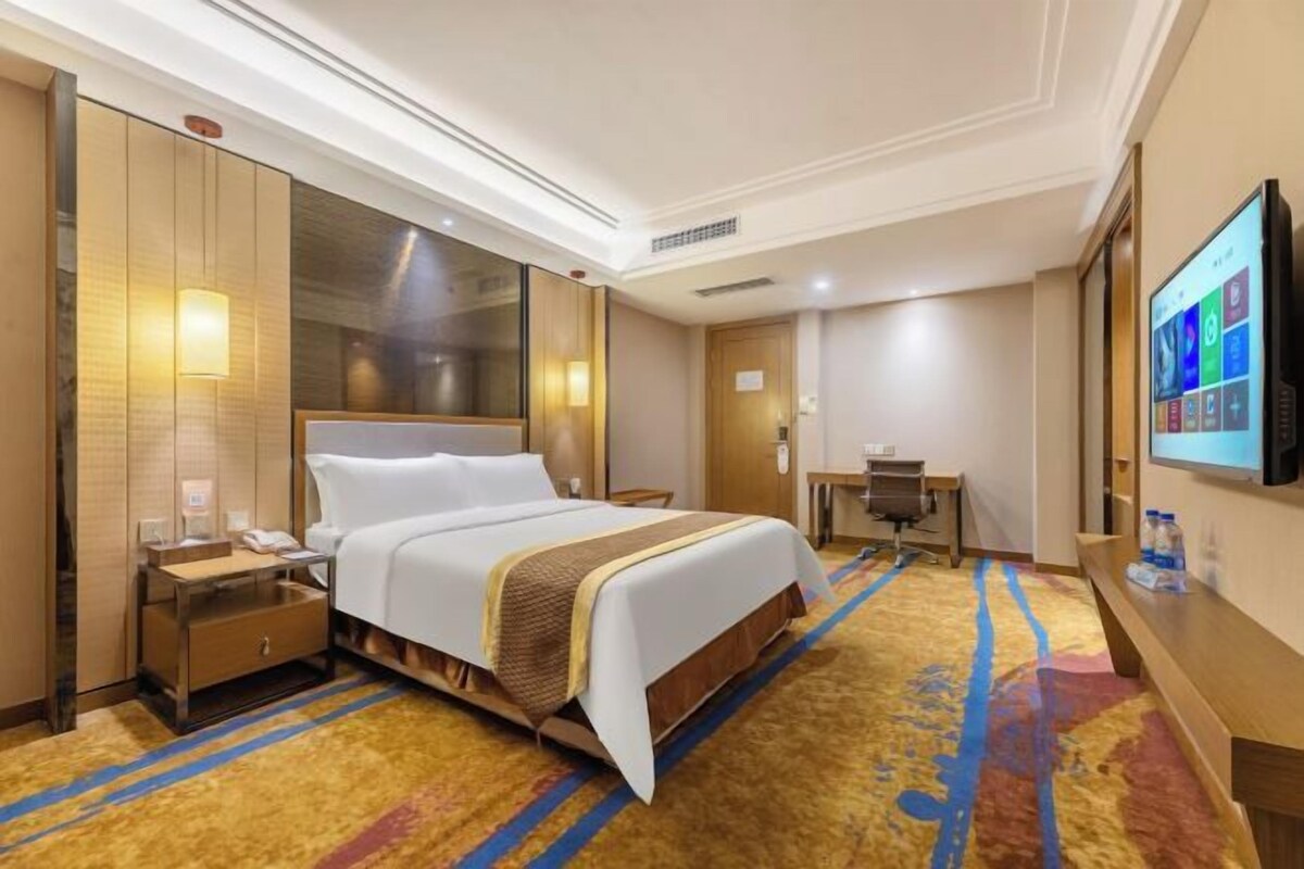 Una camera d'albergo con un letto, una scrivania, una televisione e un pavimento rivestito di moquette.