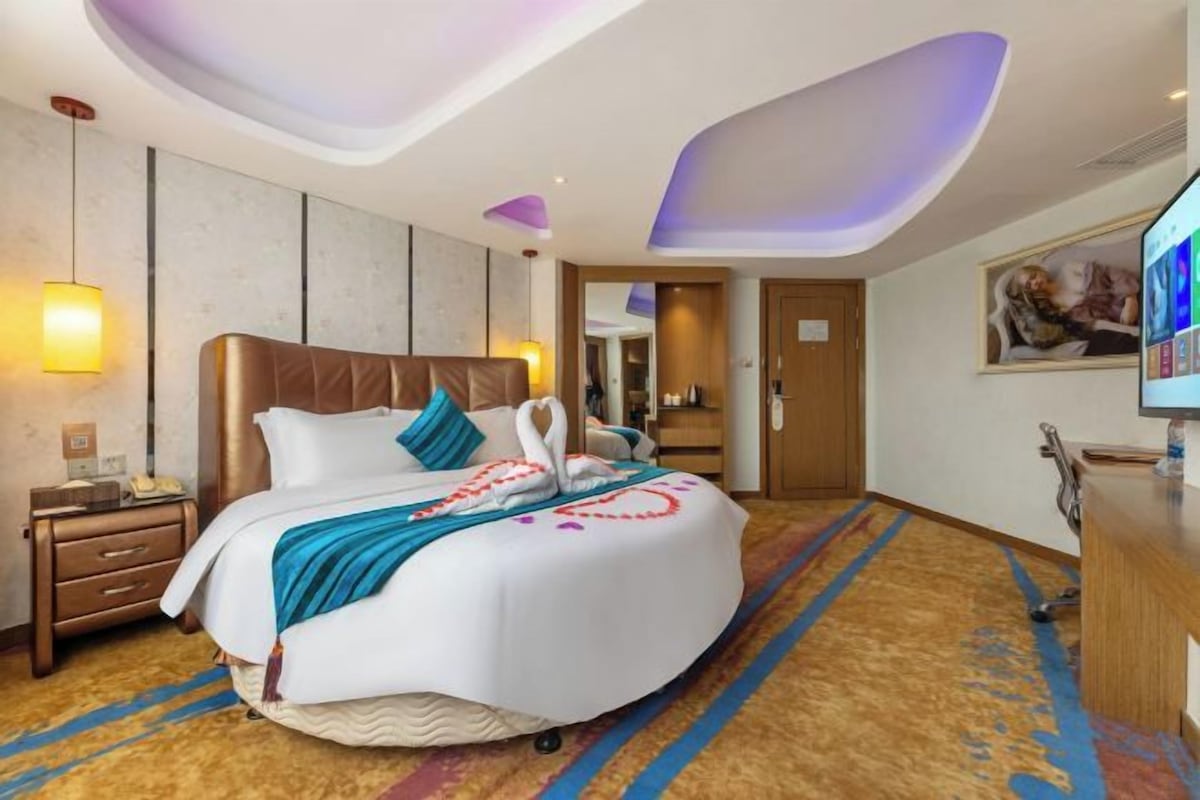 A hotel room with a large bed, a desk, a television, and a mirror.