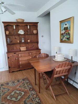 A dining area with a wooden table and chairs, a decorative cabinet with baskets, and a painting on the wall.
