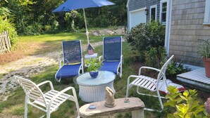 Een terras met een ronde tafel, twee blauwe stoelen en een stenen tafel met een beeldje.