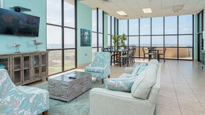Ein geräumiges Zimmer mit großen Fenstern, einem Flachbildfernseher, einem Essbereich und einer Sitzecke mit Sofa und Sesseln.