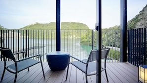 Un balcón con vistas a un lago y colinas, que incluye dos sillas y una mesa.