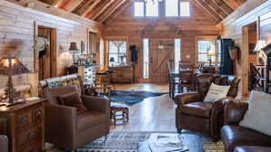 A cozy log cabin interior with a dining area, leather sofas, and a fireplace. - Whispering Falls Cabin - hot tub, views, 15 acres, minutes from Main St. (Saluda)