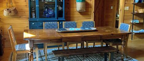 A wooden dining table with chairs, a bench, a blue cabinet with glass doors, and a patterned rug.