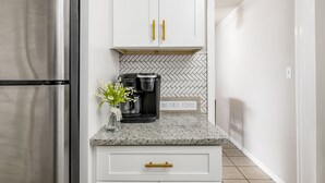 A modern kitchen with white cabinets, a stainless steel refrigerator, a coffee maker, and a herringbone-patterned backsplash.