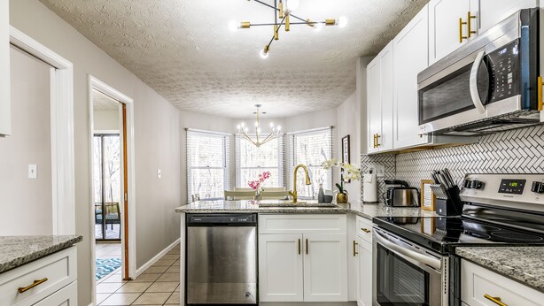 A modern kitchen with white cabinets, stainless steel appliances, and a herringbone-patterned backsplash.