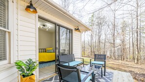 A wooden deck with a glass table and chairs, a yellow sofa inside, and a view of a forest.