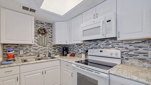 A modern kitchen with white cabinets, a microwave, an oven, and a tiled backsplash. - Caddy's #1 – Waterfront Balcony, Walk to Beach, Pet-Friendly & Next to Dining (Indian Shores)