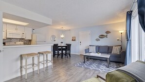 A modern kitchen with white cabinets, a dining table with chairs, a gray sofa, and a patterned rug. - Caddy's #1 – Waterfront Balcony, Walk to Beach, Pet-Friendly & Next to Dining (Indian Shores)