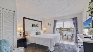 A bedroom with a bed, bedside tables, a desk, and a balcony with a view. - Caddy's #1 – Waterfront Balcony, Walk to Beach, Pet-Friendly & Next to Dining (Indian Shores)