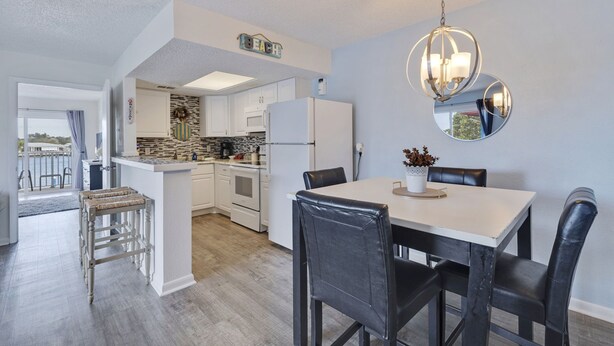 A modern kitchen with white cabinets, a central island, and a dining area with a white table and black chairs. - Caddy's #1 – Waterfront Balcony, Walk to Beach, Pet-Friendly & Next to Dining (Indian Shores)