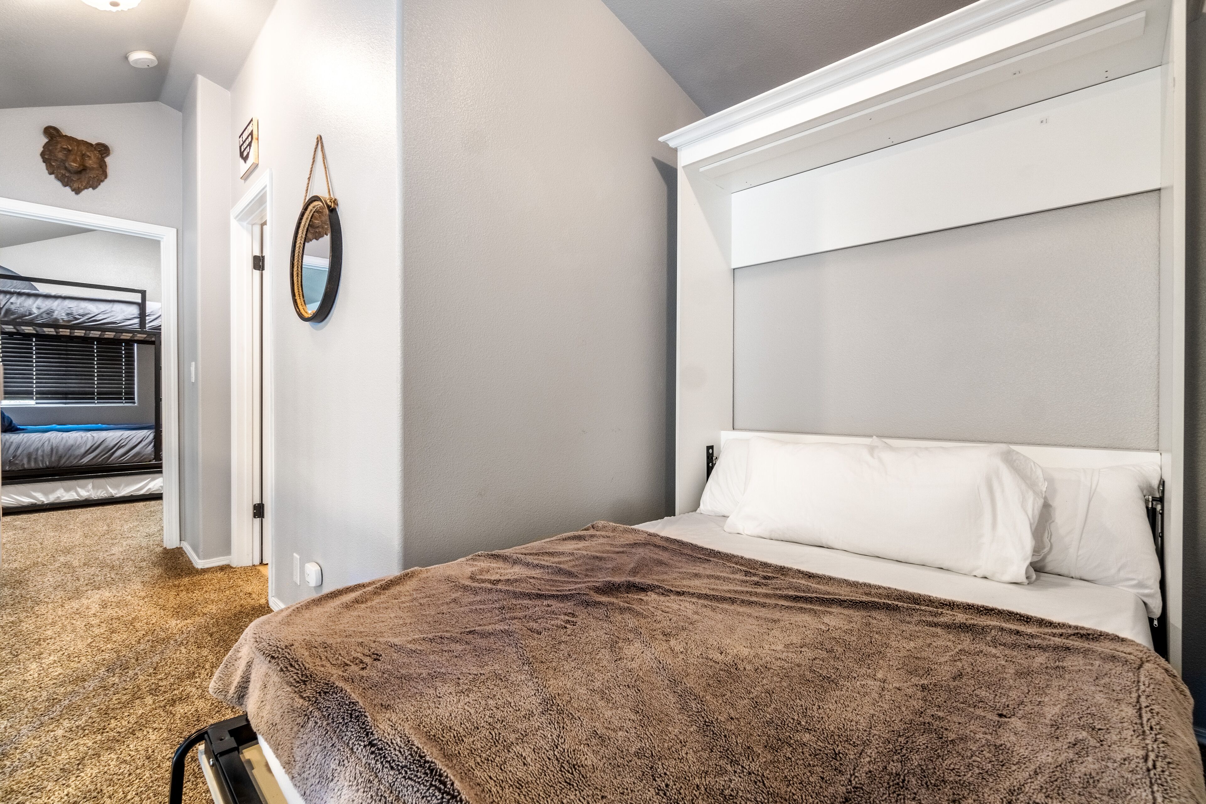 Ein Schlafzimmer mit einem großen Bett, einem Kopfteil, einem Spiegel und einer Tür zu einem anderen Raum.