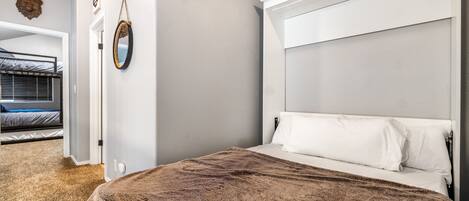 Ein Schlafzimmer mit einem großen Bett, einem Kopfteil, einem Spiegel und einer Tür zu einem anderen Raum.