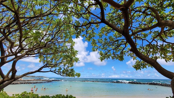 A beach with clear water, rocky shore, and people swimming.