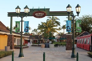 L'entrée du centre commercial Coconut Marketplace, avec un panneau indicateur, des lampadaires et des banderoles faisant la publicité de concerts et d'un marché de producteurs.
