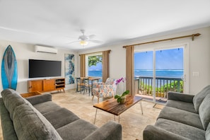 A living room with a TV, sofa, coffee table, and a view of the ocean.