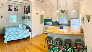 A compact, well-lit room with a bed, a kitchenette, and a small bar area. - The Surf Cottage - Beach and Jungle all in One!  An off the grid cottage. (Gregory Town)