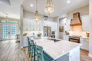 A spacious kitchen with white cabinets, a large island with bar stools, stainless steel appliances, and pendant lighting. - Waterfront Key West Style Home with Heated Pool Located in South Gulf Cove (Port Charlotte)