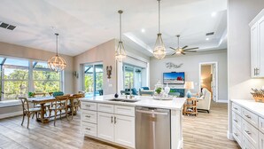 Una cocina amplia con armarios blancos, una isla central y un comedor con sillas de madera.