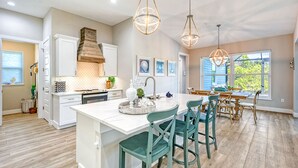Una cocina moderna con una isla grande, luces colgantes y un comedor con sillas de madera.