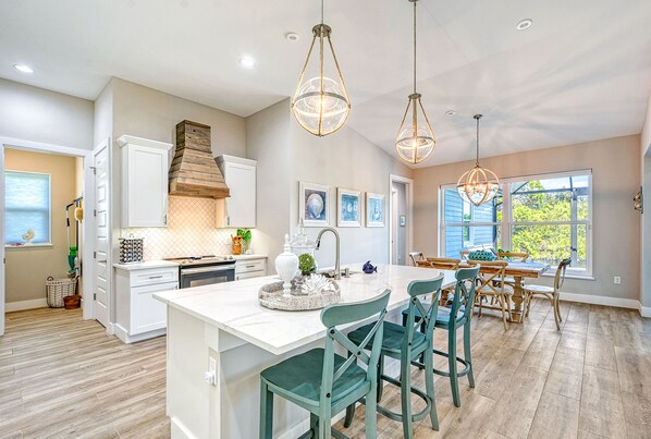 A modern kitchen with a large island, pendant lights, and a dining area with wooden chairs. - Waterfront Key West Style Home with Heated Pool Located in South Gulf Cove (Port Charlotte)