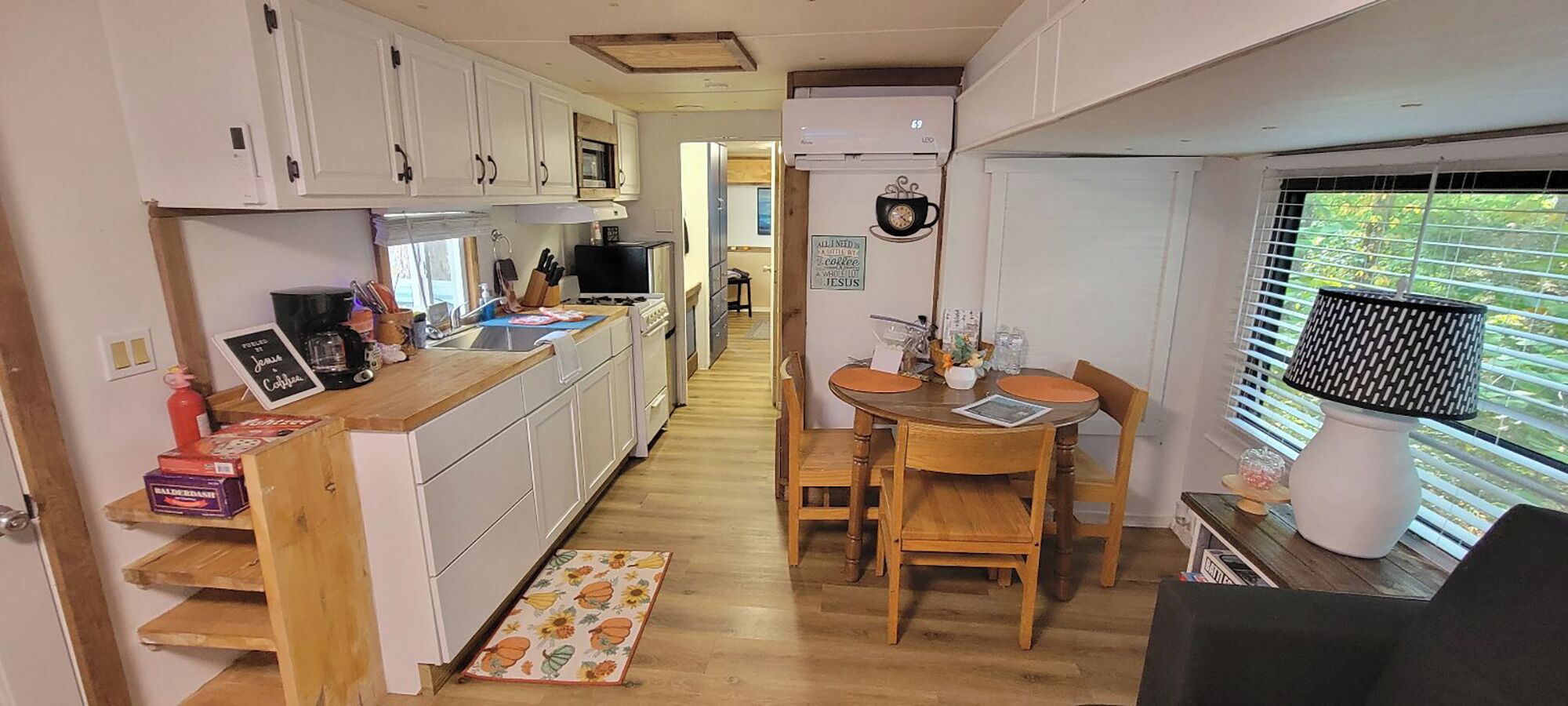 Une cuisine compacte avec des meubles blancs, un plan de travail en bois et un coin repas comprenant une table et des chaises.