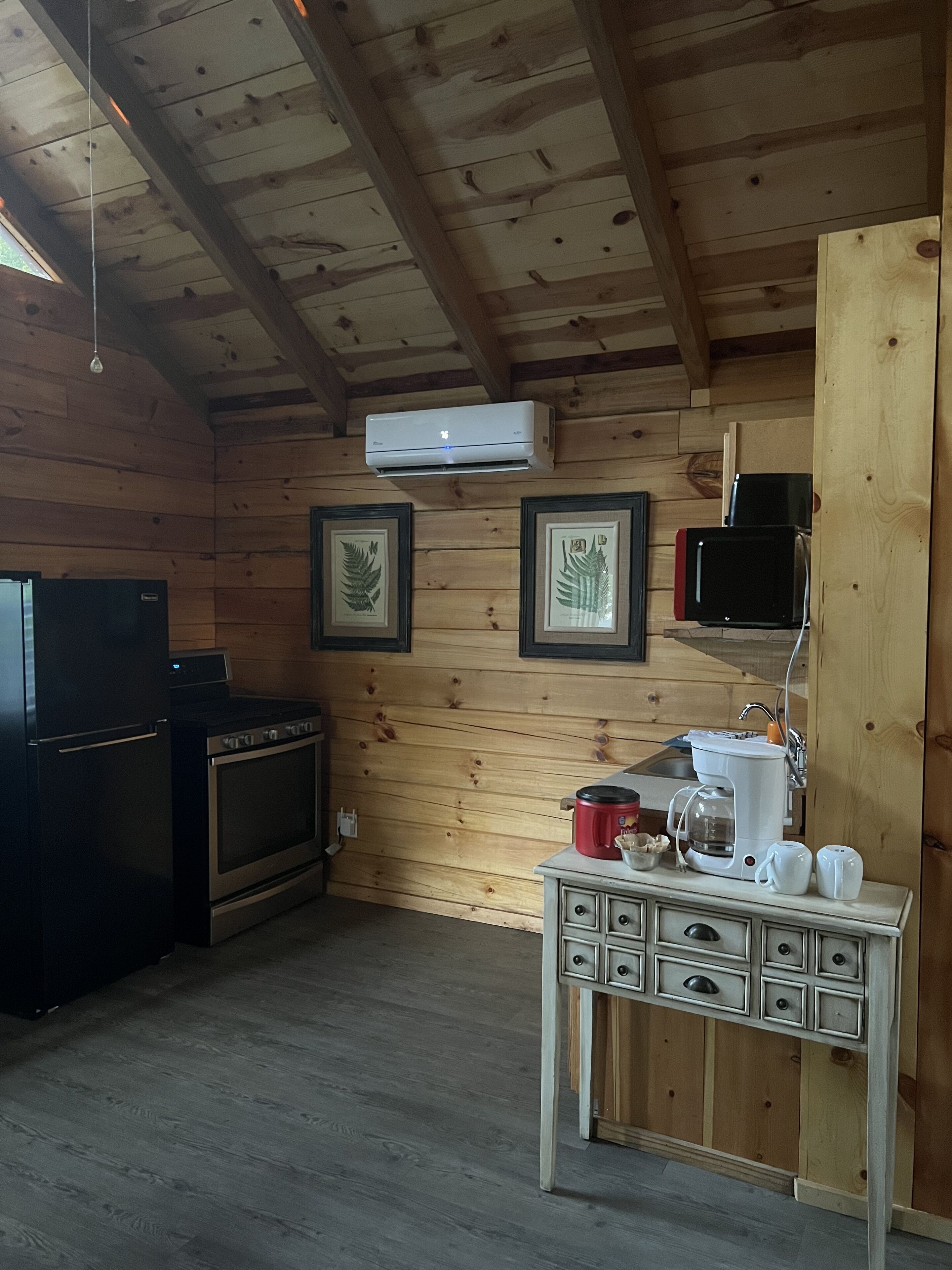 A wooden cabin kitchen with a stove, refrigerator, and a coffee maker on a wooden table.