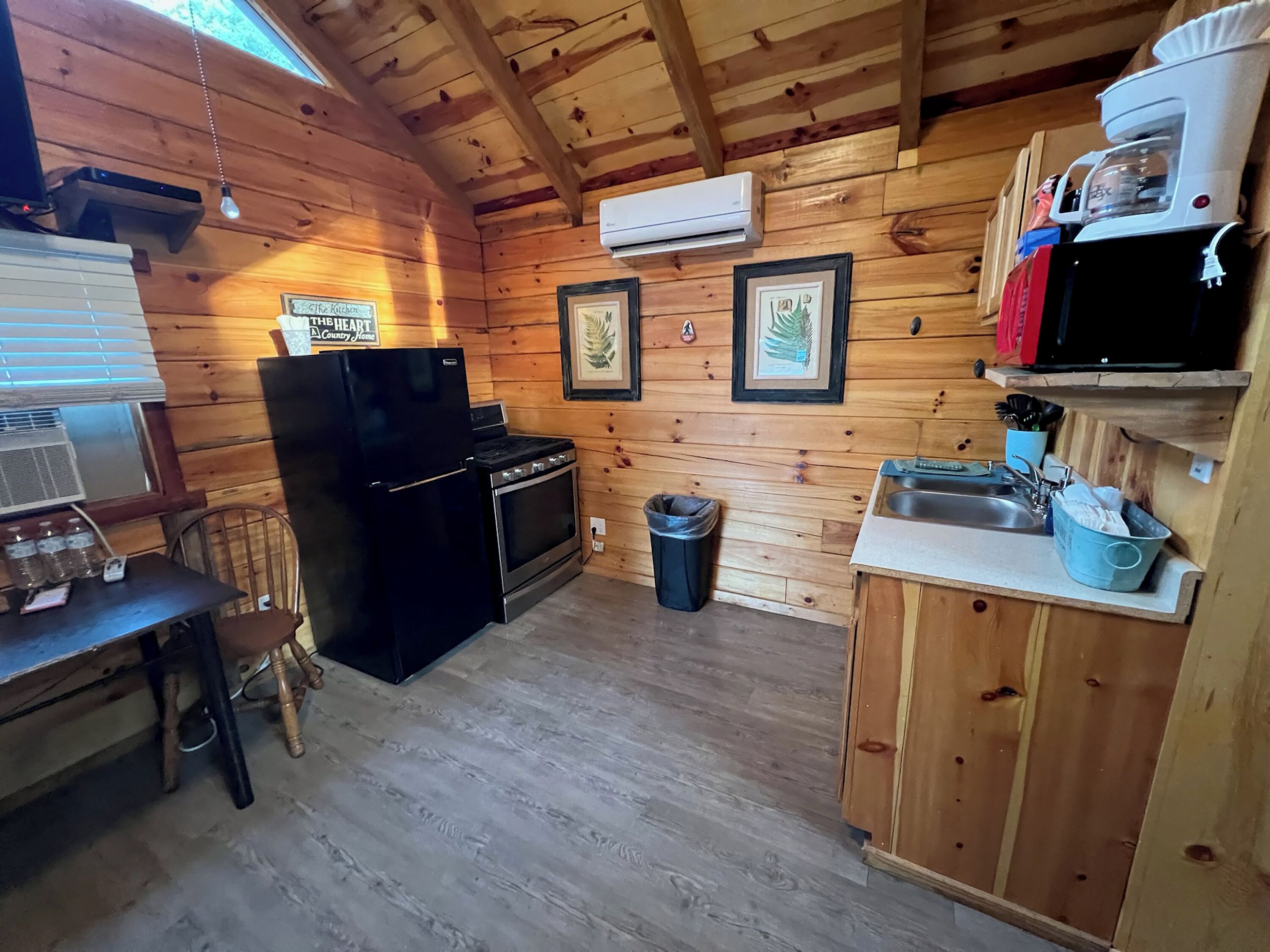 A wooden cabin kitchen with a refrigerator, stove, sink, and a coffee maker on the wall.