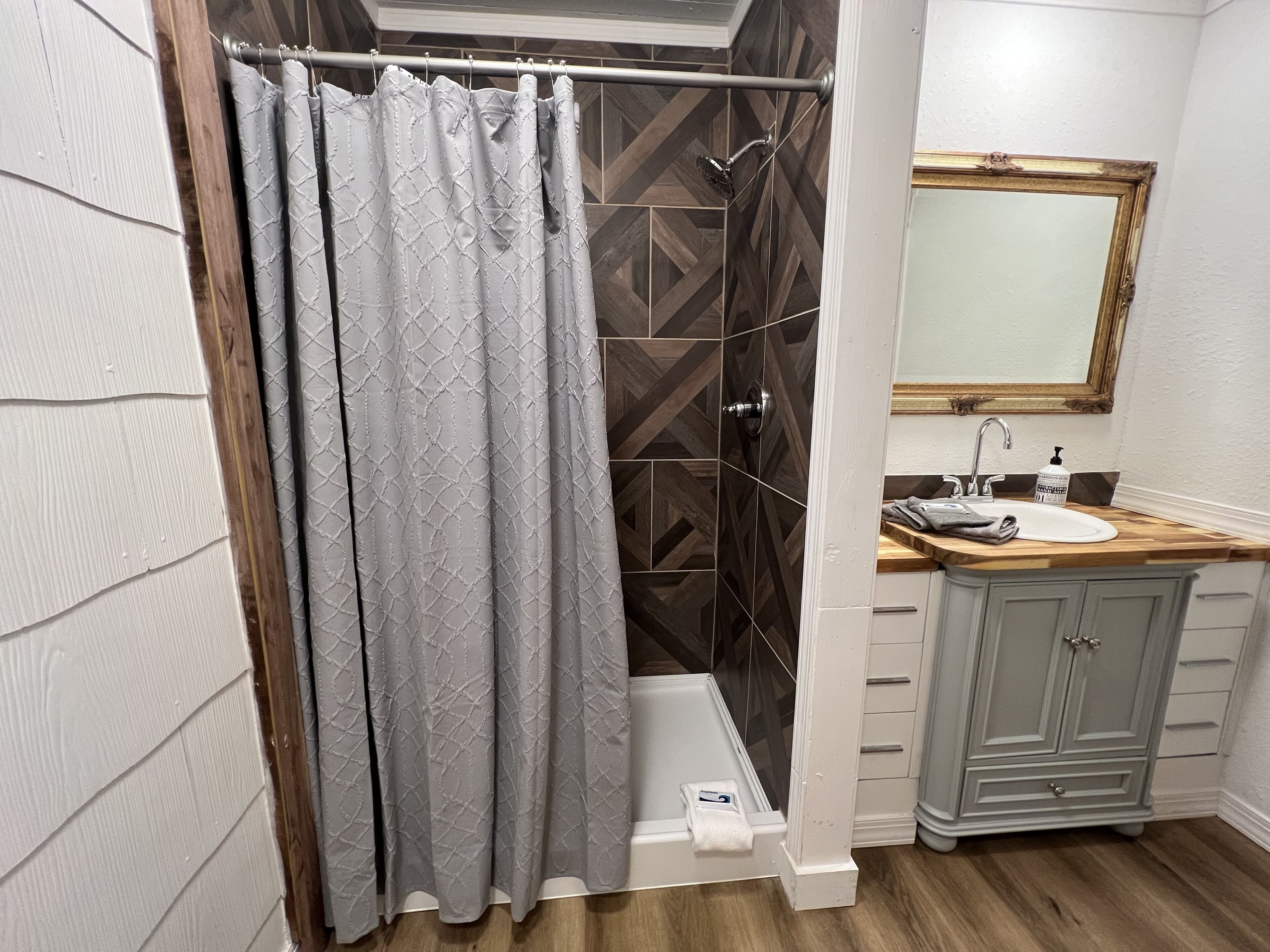 Une salle de bain avec un rideau de douche, une baignoire, un lavabo avec un miroir et un plancher en bois.