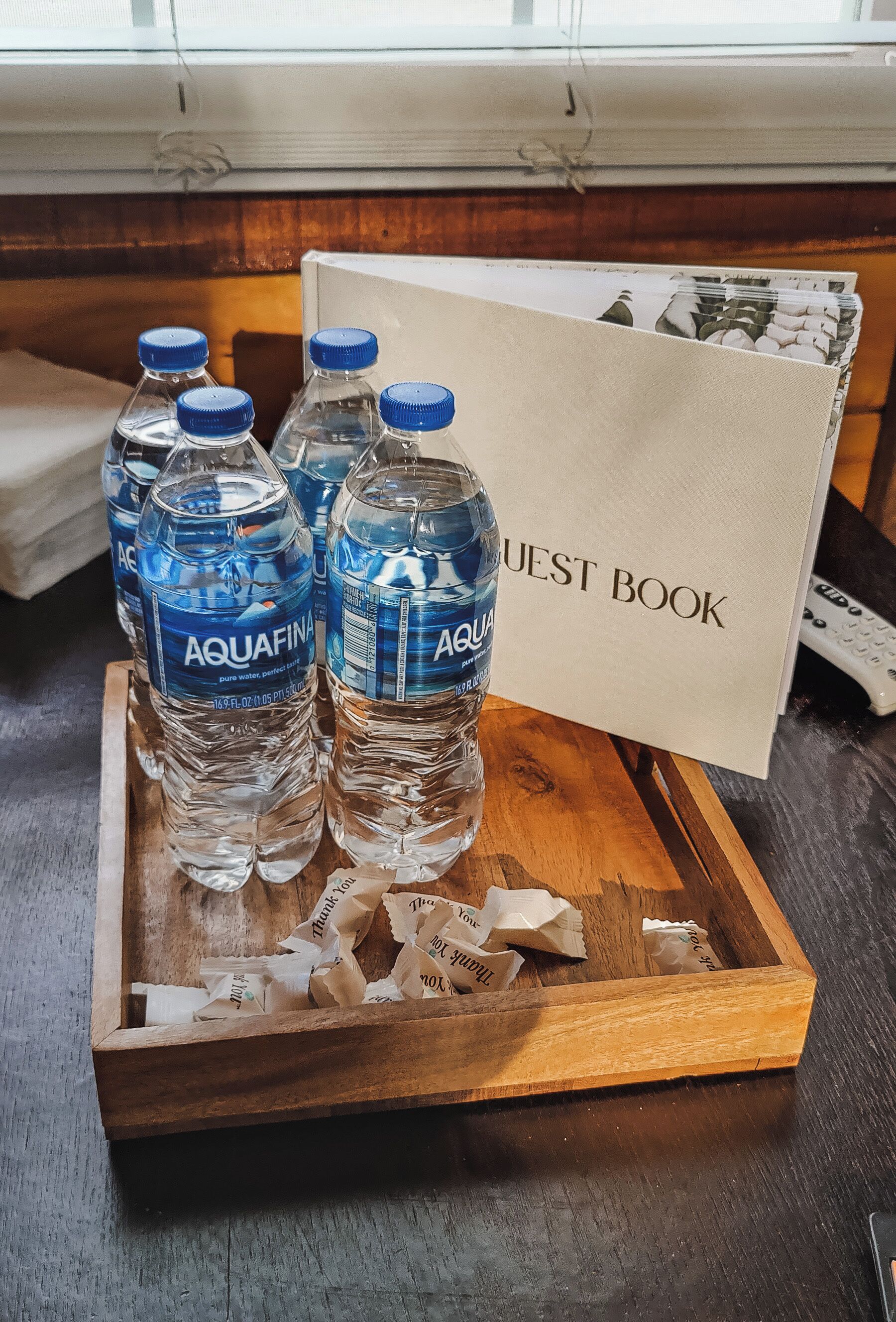 A wooden tray with bottles of Aquafina water and a guest book on a wooden table.
