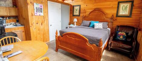 A wooden cabin bedroom with a bed, a wooden table, a chair, and a desk with kitchen appliances.
