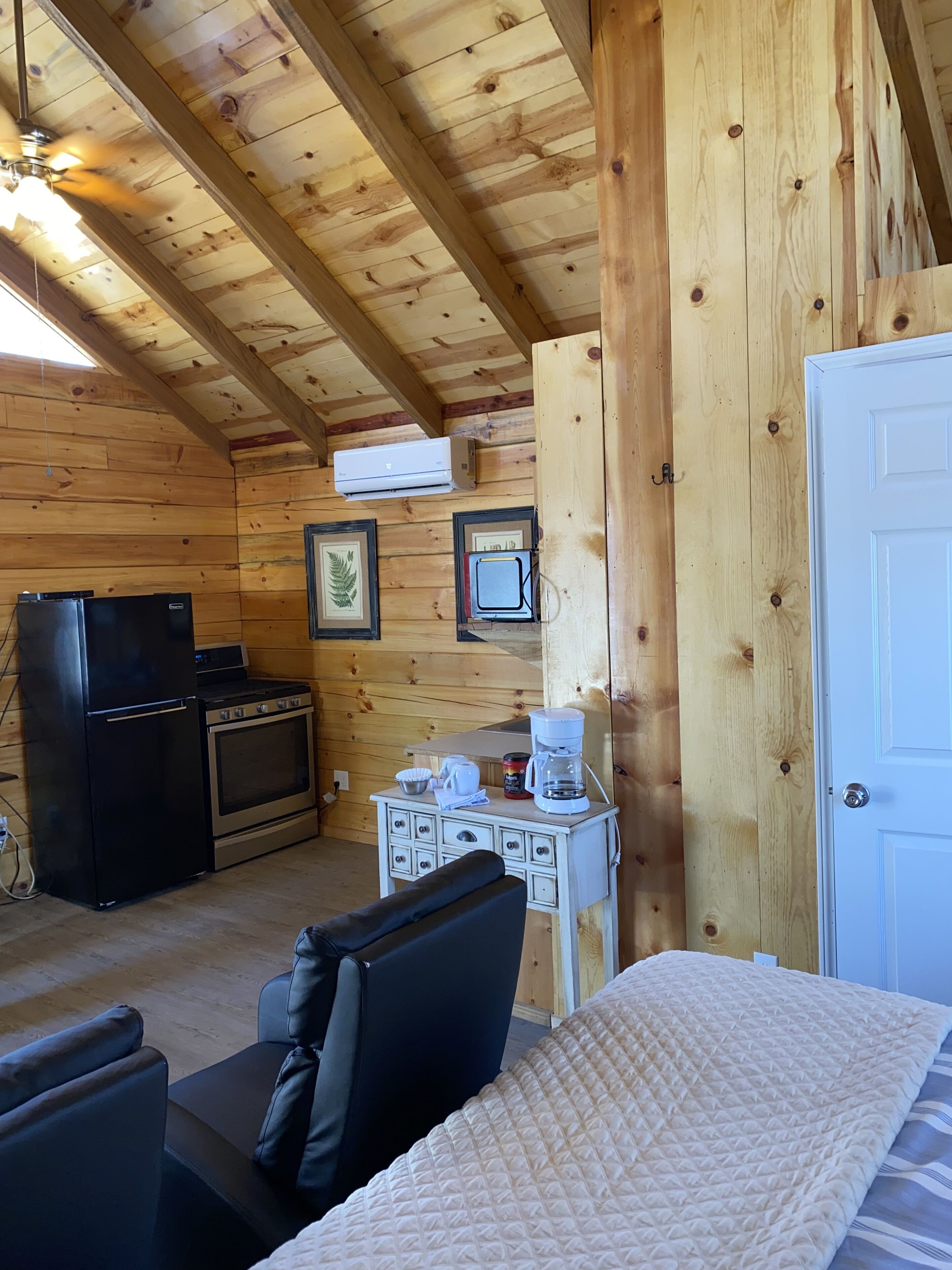 A cozy cabin interior with wooden walls, a kitchenette, a bed, and a ceiling fan.