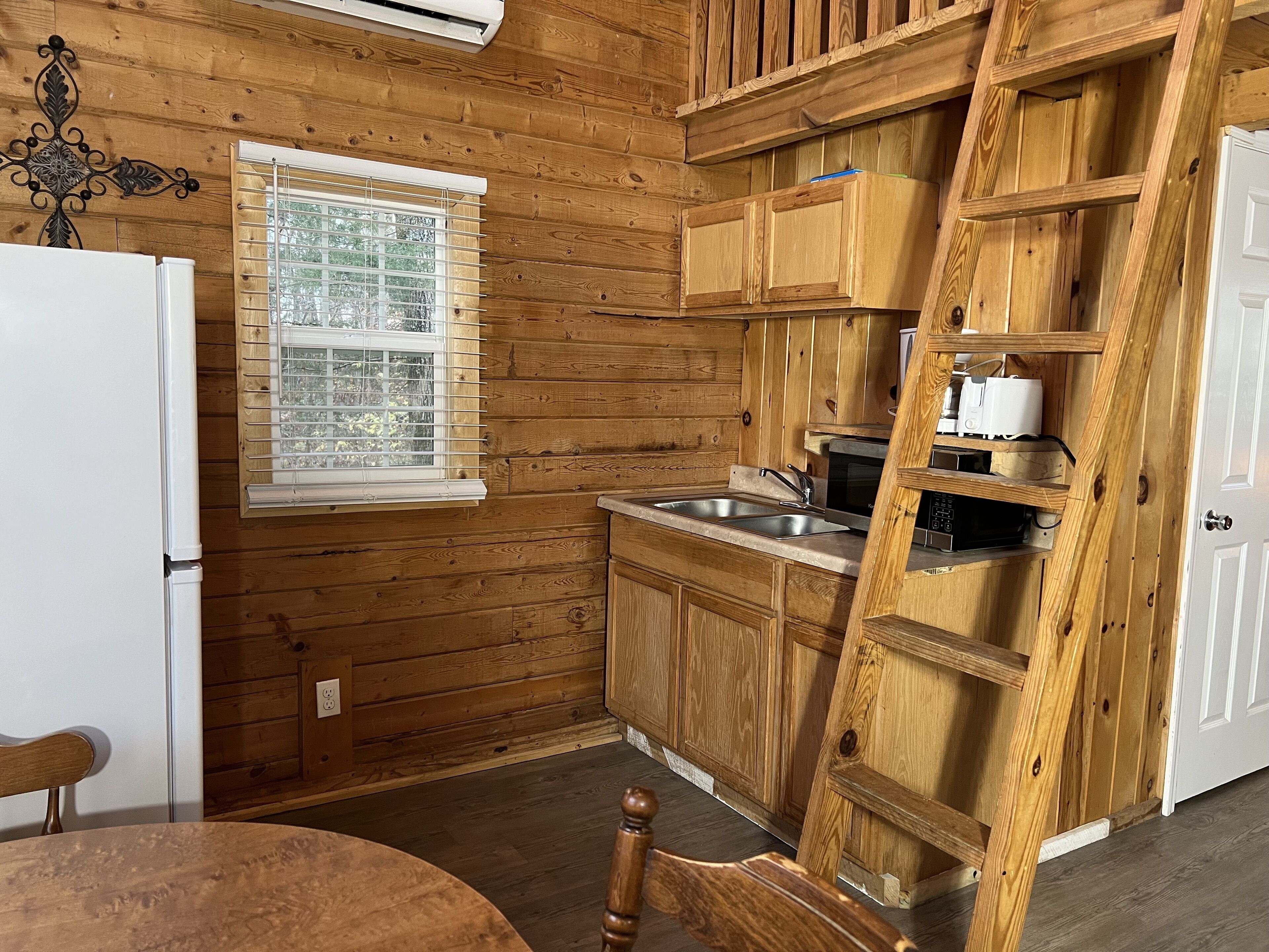 Interior de una cabaña de madera con cocina, que incluye un refrigerador, pileta y armarios de madera.