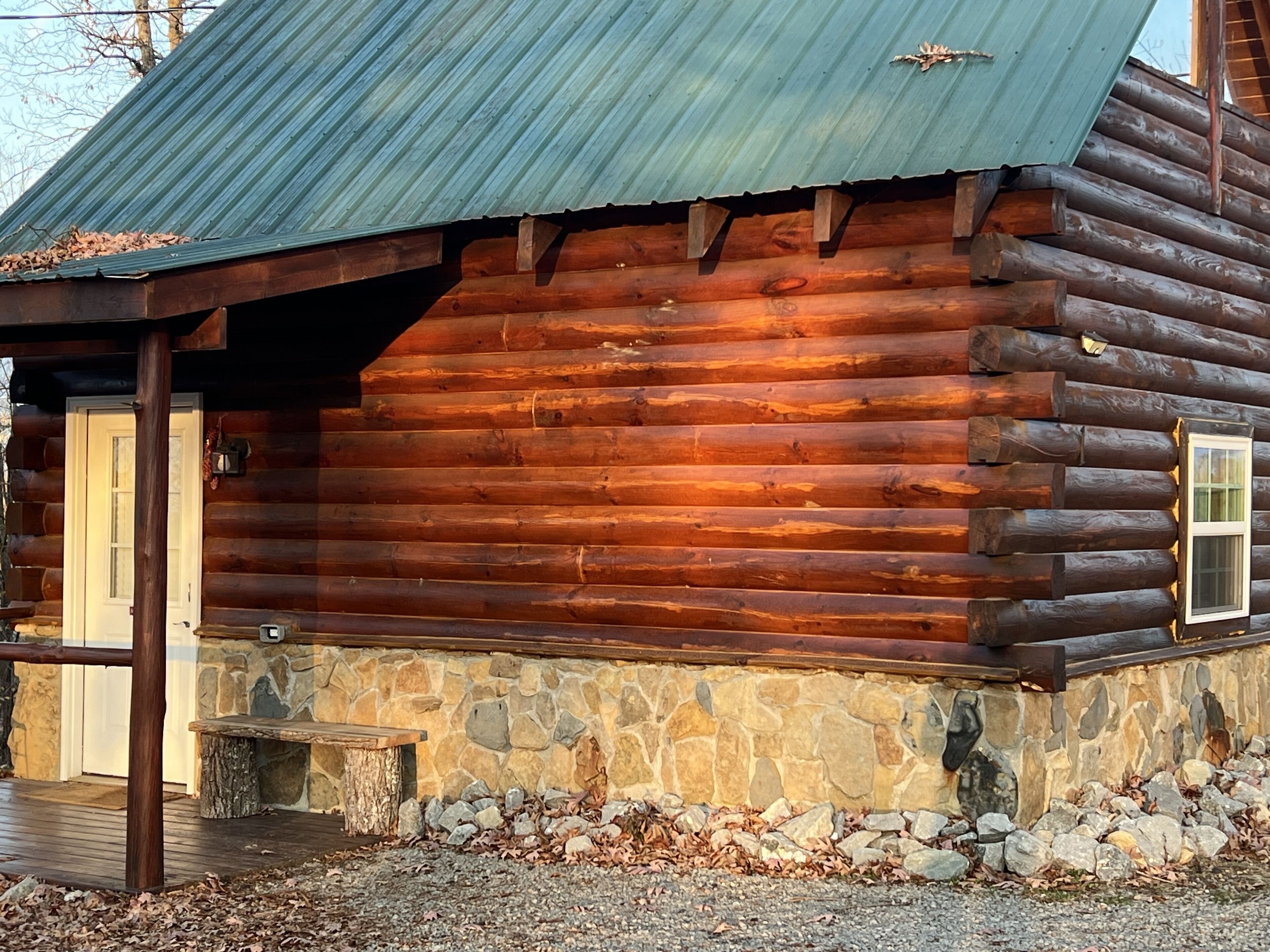 A log cabin with a stone foundation, a wooden door, and a metal roof.