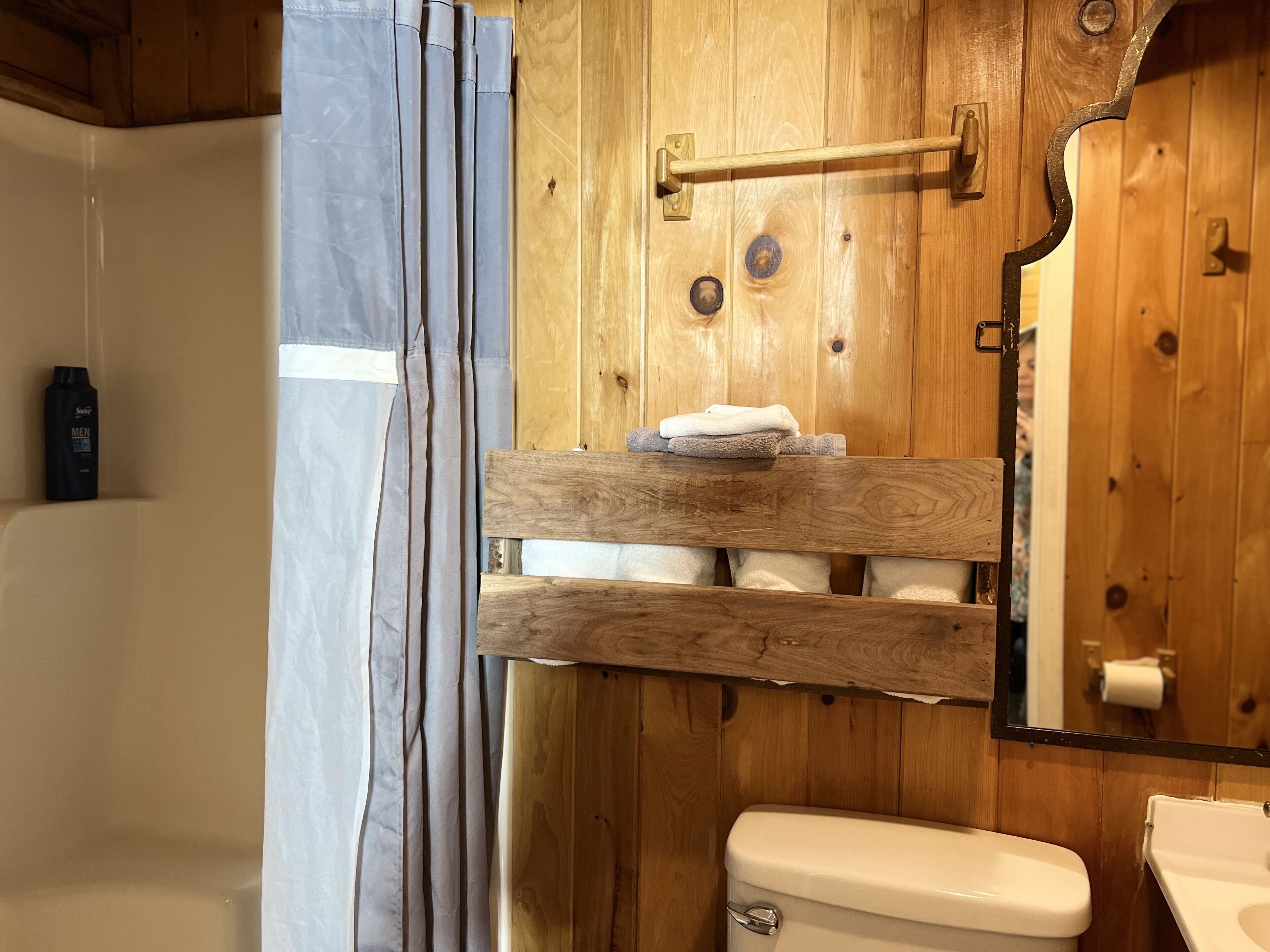 A wooden bathroom with a toilet, a towel rack, and a shower curtain.