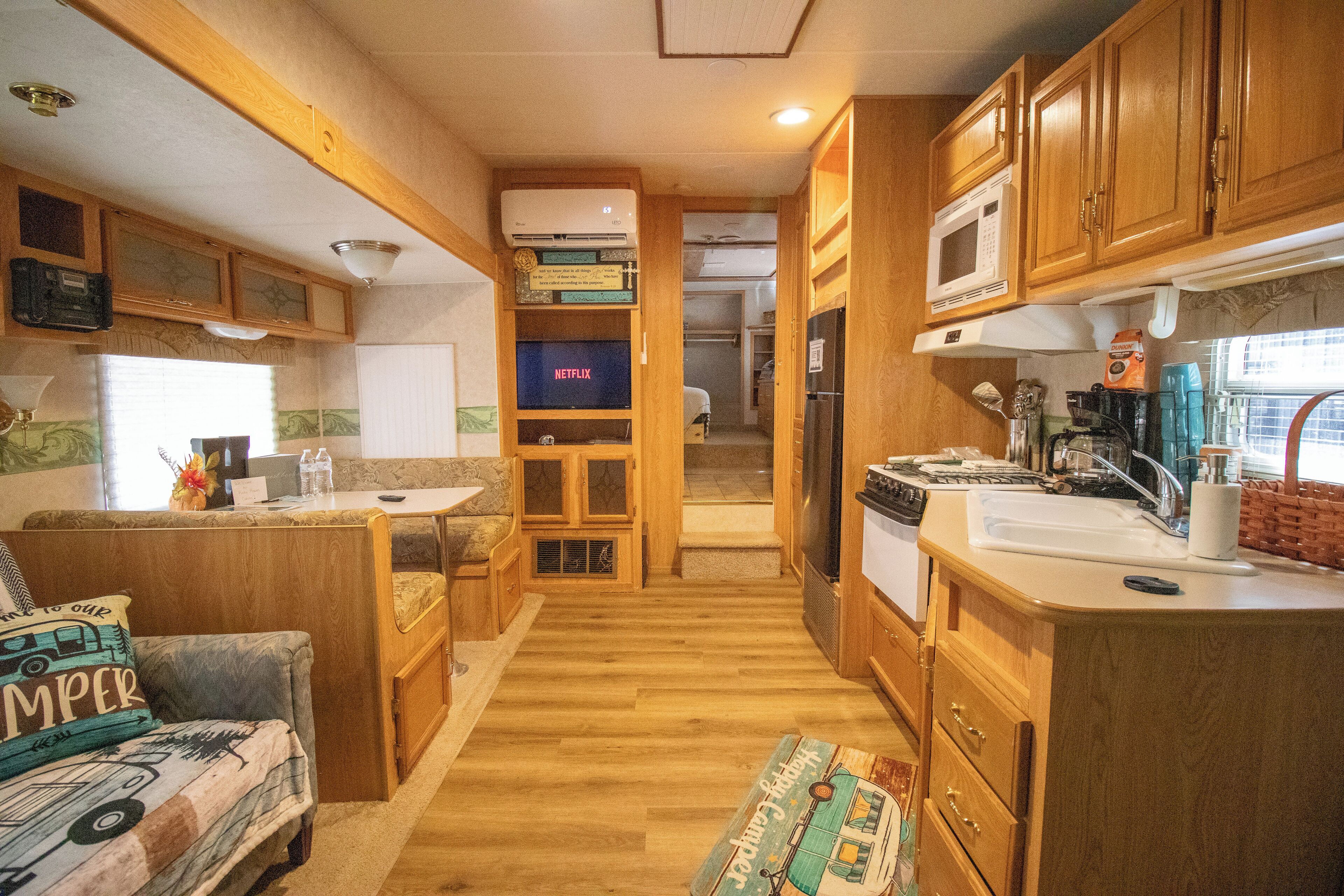 Een compacte RV-keuken met houten kastjes, een magnetron, een spoelbak en een eethoek met een kleine tafel en stoelen.