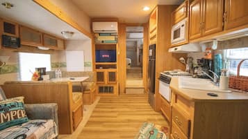 Een compacte RV-keuken met houten kastjes, een magnetron, een spoelbak en een eethoek met een kleine tafel en stoelen.