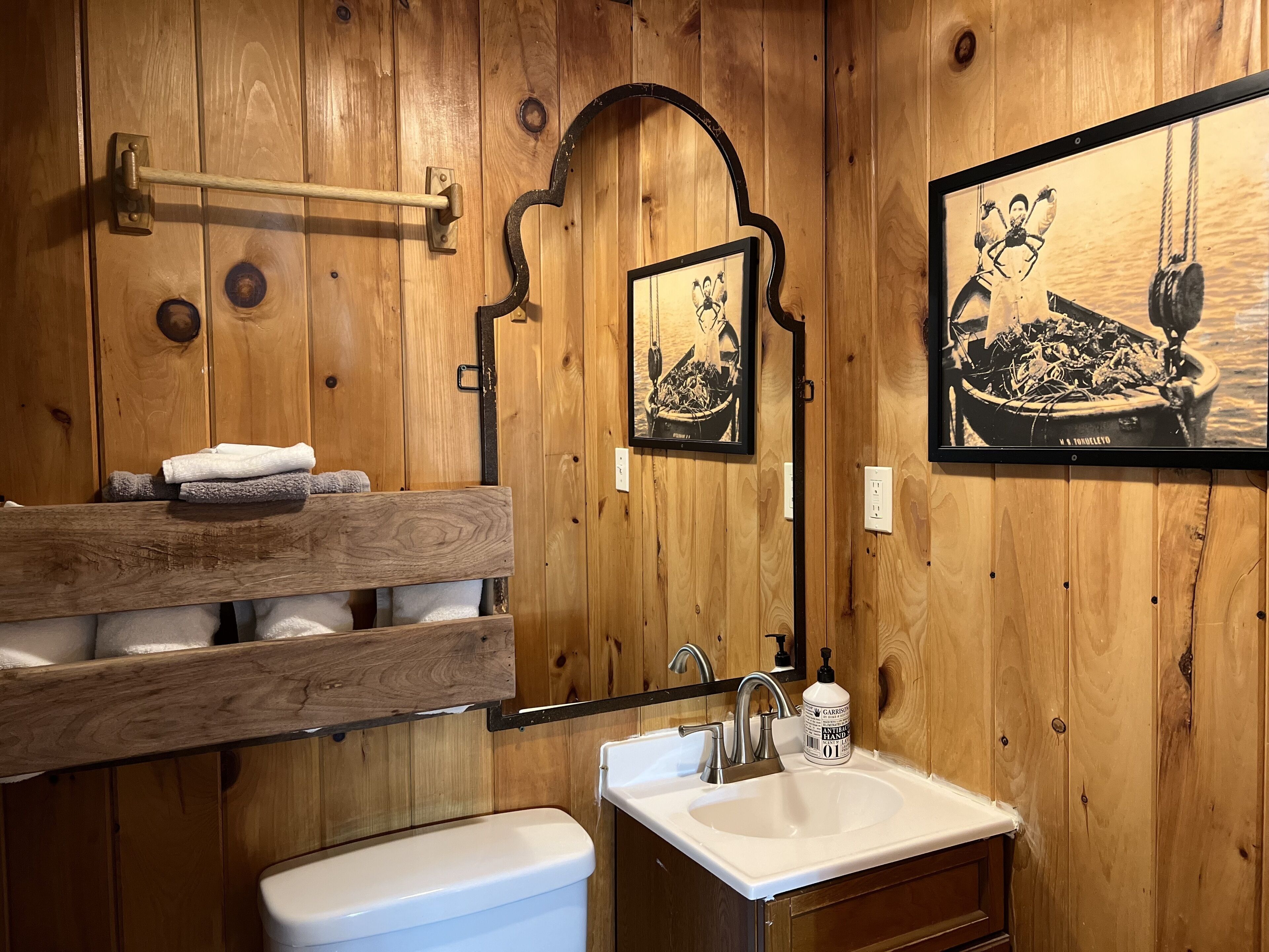 Un baño con paneles de madera, que incluye un inodoro, lavamanos, toallero y dos cuadros enmarcados.