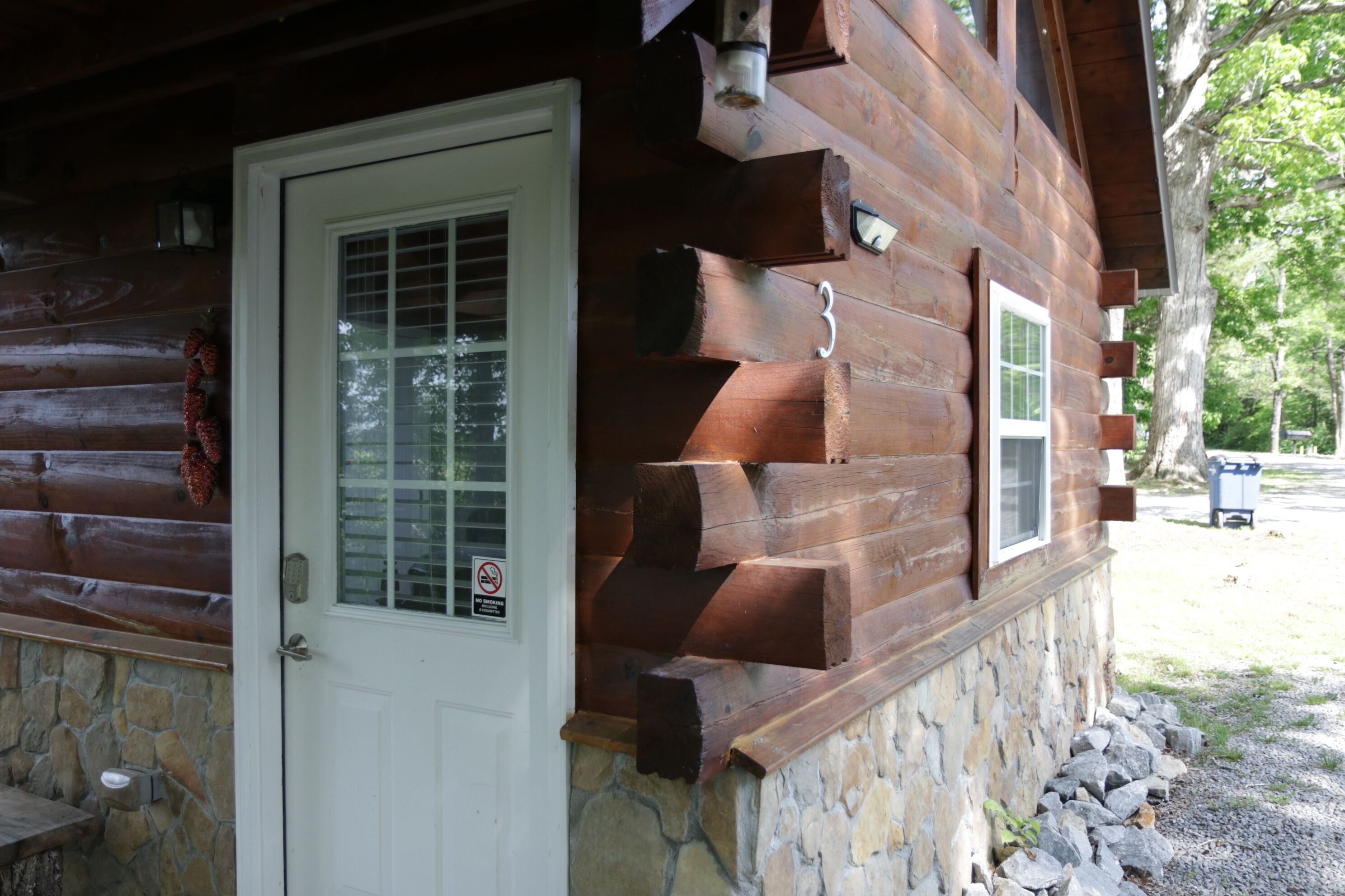 A log cabin with a stone foundation, a white door, and a small porch area.