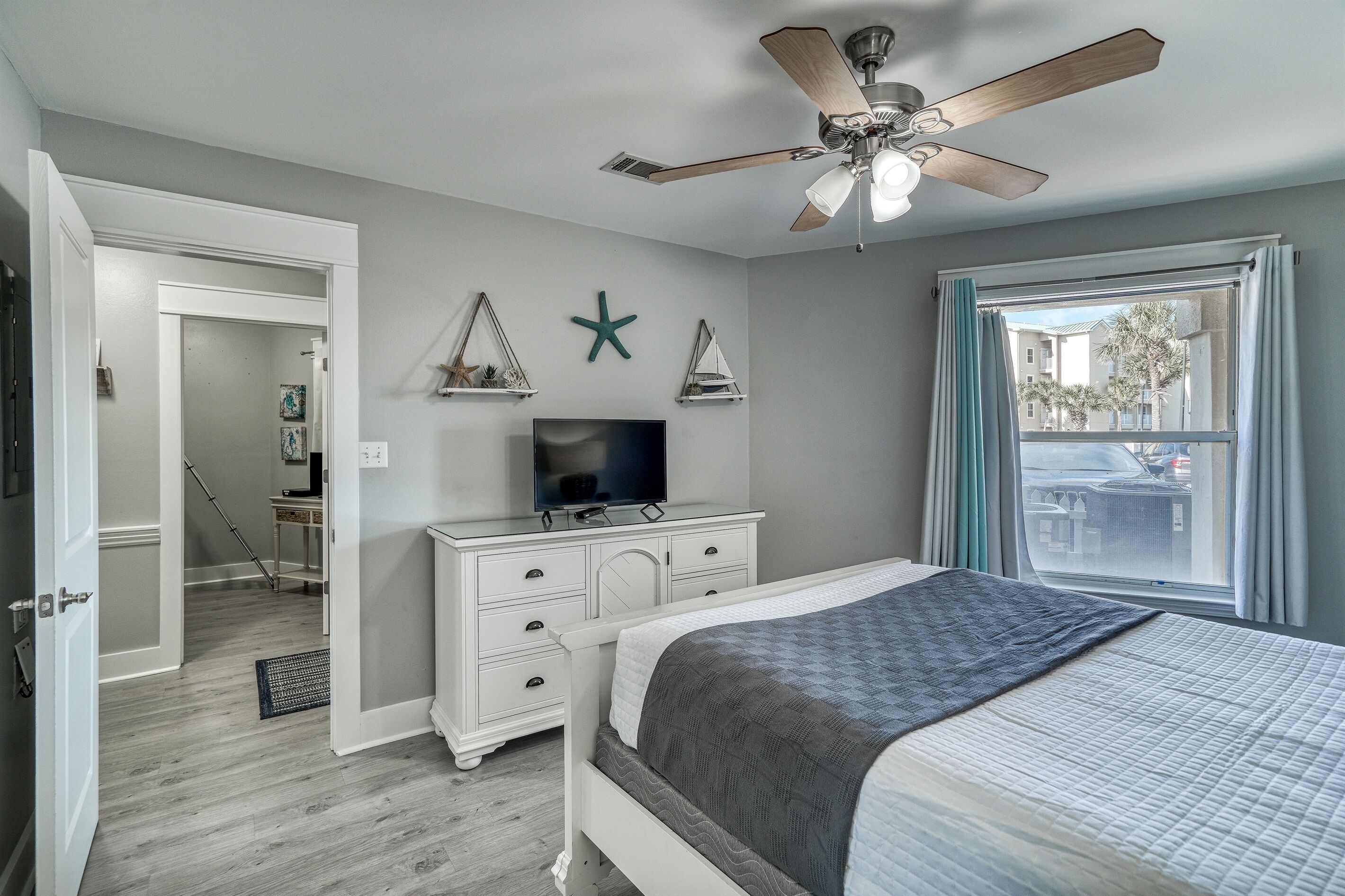 A bedroom with a bed, a ceiling fan, a TV, and a window with curtains.