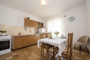A kitchen with wooden cabinets, a dining table with chairs, a clock on the wall, and a window with curtains.