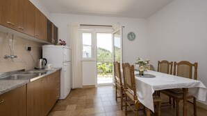 A kitchen with wooden cabinets, a sink, and a dining area with a table and chairs. - Spacious apartment w. balcony, big garden & grill (Podglavica)