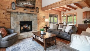 A cozy living room with a stone fireplace, wooden beams, and a stone wall. - Amazing Wild Escape!-3Full Baths,Game,Hot Tub,Pets (Sevierville)