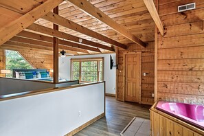 A wooden cabin interior with a large window, a wooden deck, a hot tub, and a door.