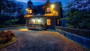 A two-story wooden house with a porch, surrounded by a fence and trees. - Amazing Wild Escape!-3Full Baths,Game,Hot Tub,Pets (Sevierville)