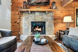 A cozy living room with a stone fireplace, a flat-screen TV above it, and comfortable seating.