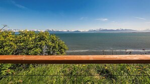 Une vue sur un lac, avec des montagnes en arrière-plan, une clôture en bois au premier plan et de la végétation tout autour.
