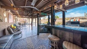 Ett takförsett utomhusområde med sittplatser, en bar, stolar och en skylt som visar att det är "ÖPPET".