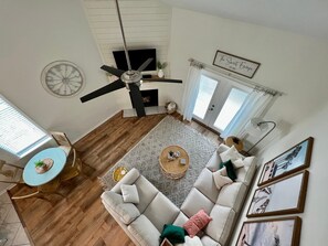 A spacious living room with a ceiling fan, a fireplace, a large window, and a dining area with a table and chairs.
